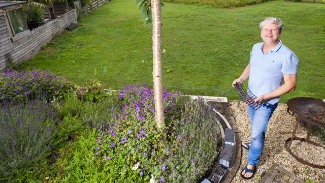 Modeltreinfanaat Henri in zijn tuin met een spoor in zijn hand.