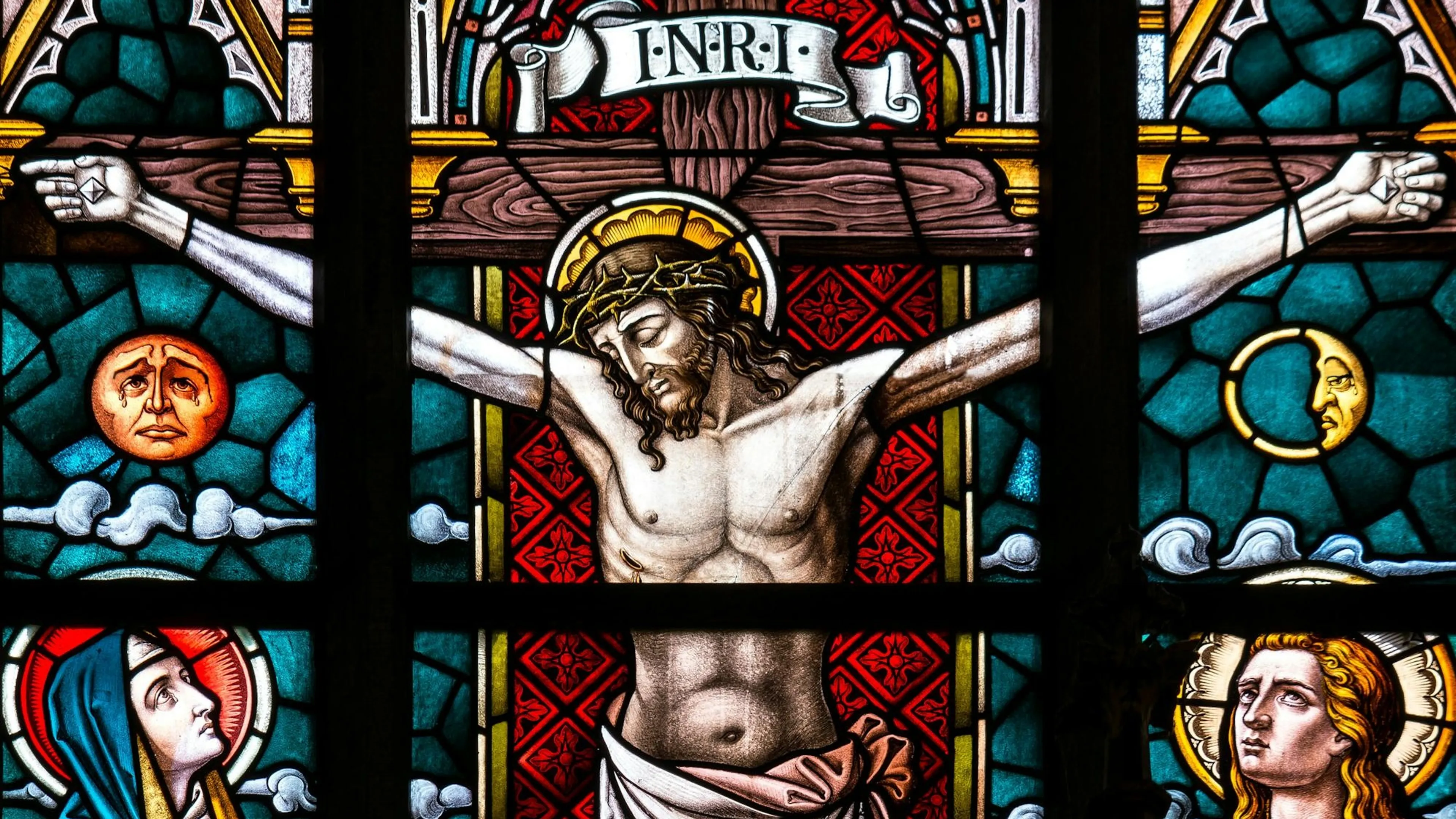 Glas-in-loodraam met een afbeelding van Jezus aan het kruis, met touwen om Zijn armen en spijkers door Zijn handen. Hoogstwaarschijnlijk werd Hij – zoals iedere gekruisigde – door de Romeinen volledig naakt aan het kruis vastgemaakt, als ultieme vernedering.