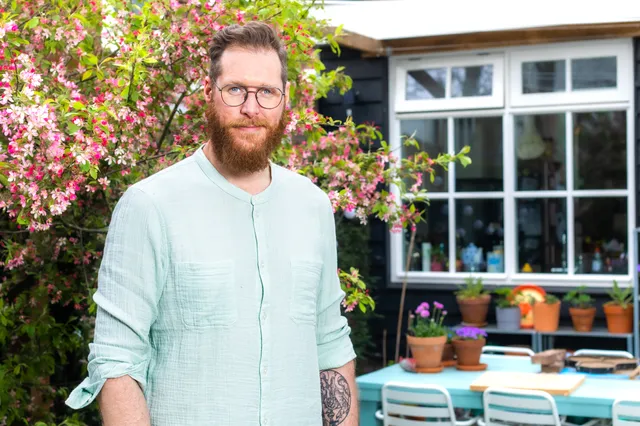 Bert Bos met achter hem ramen en een tuinset.